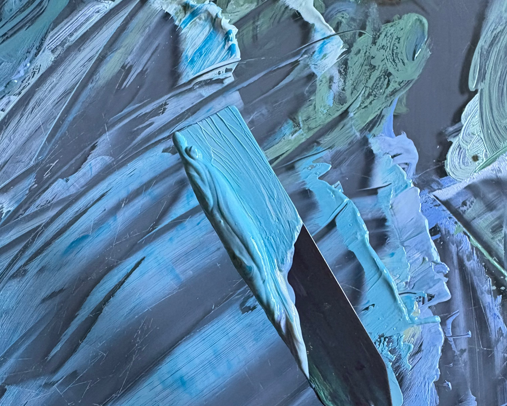 Close-up of a paintbrush with blue and green paint strokes on a textured surface.